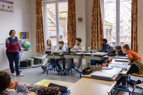 Des élèves en classe d'ULIS sont assis en classe et écoutent l'enseignante parler.
