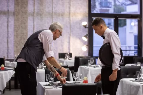 Un jeune en formation accompagné de son formateur en train de dresser une table 